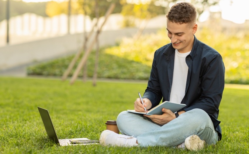 Junger-Mann-sitzt-mit-Laptop-auf-Rasen 