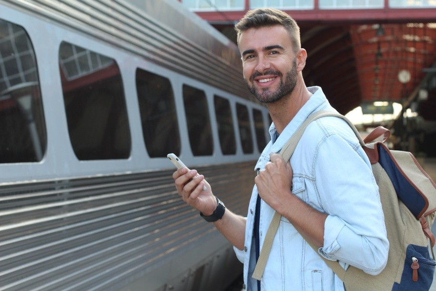 Junger Mann steht mit Handy und Rucksack am Bahnsteig - Hemd knitterfrei transportieren